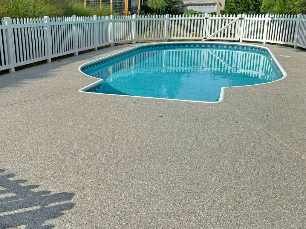 Residential pool area featuring a coated concrete pool deck and surrounding white fence.