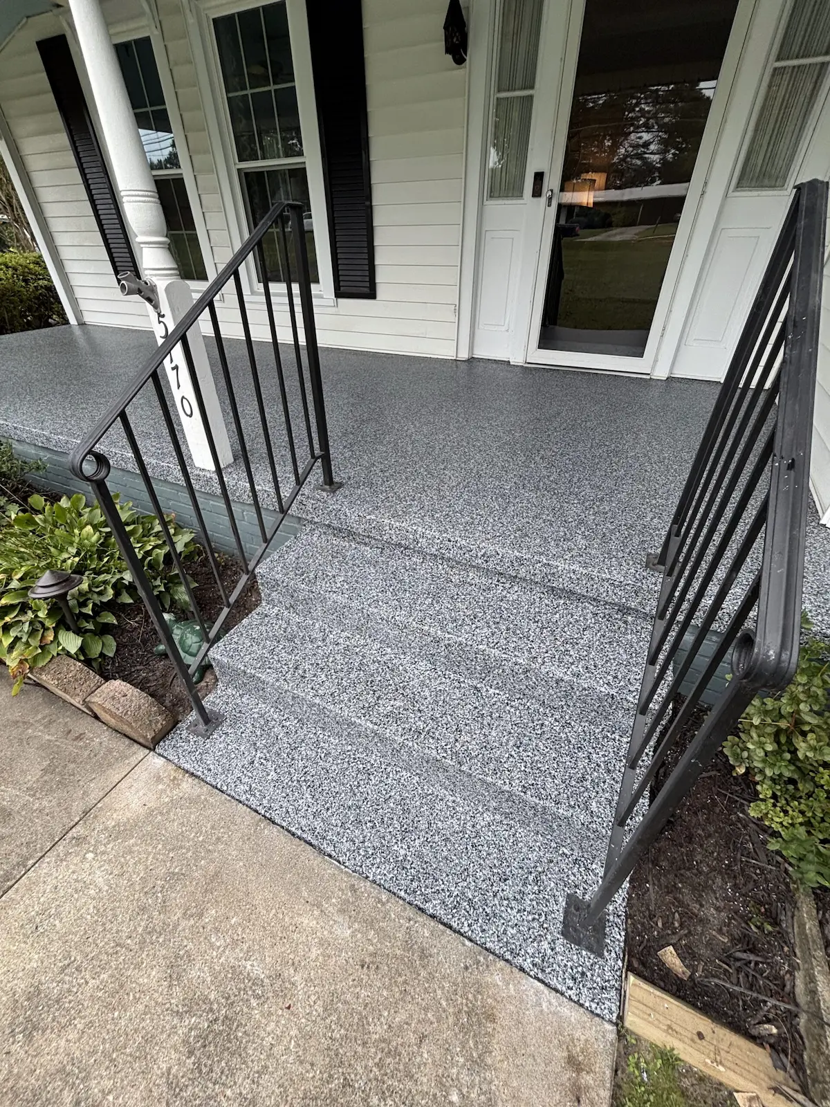 A front porch that has three stairs and railing with a professional concrete coating on the porch and stairs.