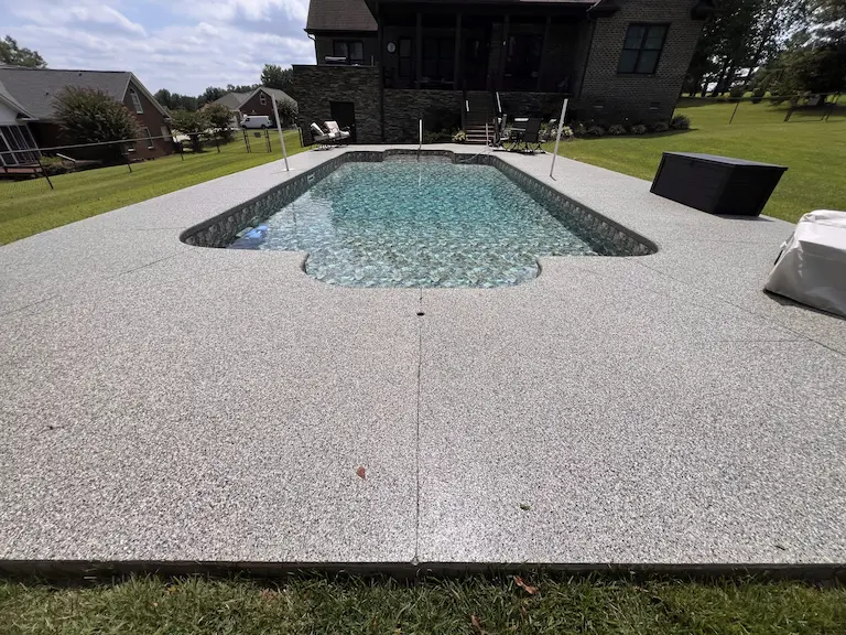 An in-ground residential backyard swimming pool with a new concrete coating surrounding the pool.