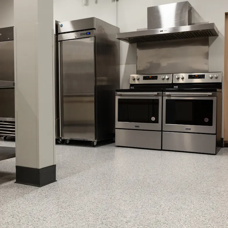 A commercial kitchen floor coated in stargazer with two stainless steel commercial ranges and storage.